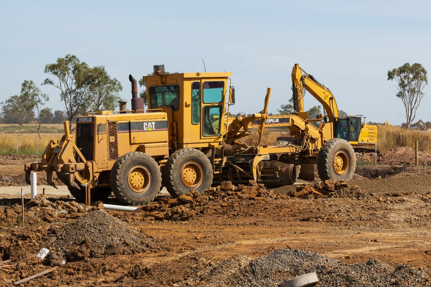 Caterpillar motor grader and excavator shaping ground on an earthworks site